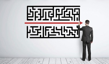 Man stands in front of a picture of a maze and has drawn a red line through the centre of it.