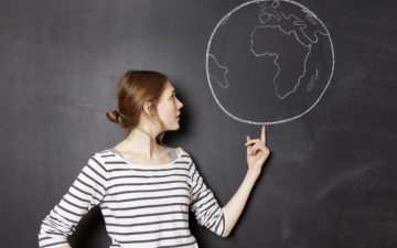 A woman standing in front of a blackboard pointing to a drawing of the earth