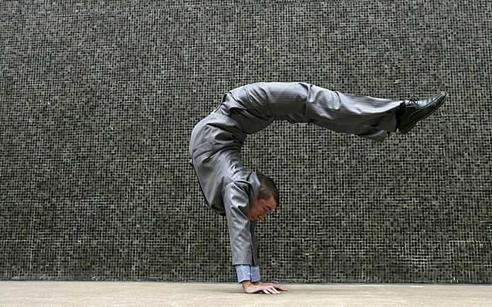 Businessman in a grey suit doing a handstand outdoors