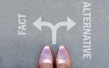 A pair of shoes at a crossroads, one side labelled fact and one side labelled alternative