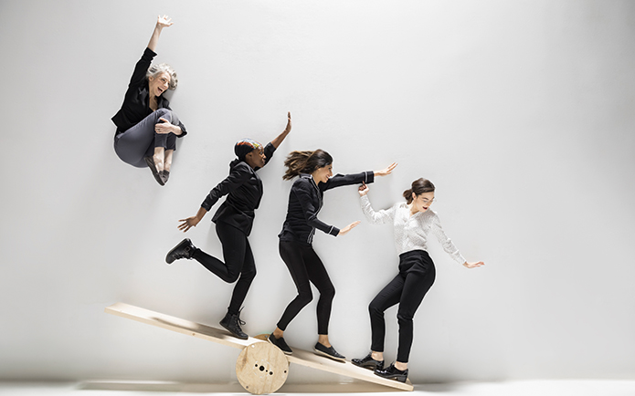 Four women balancing on a wooden teeter-totter